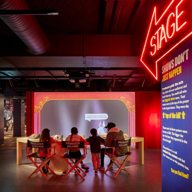 Inside the Showtime gallery at Showtown.  A neon sign points to the stage and a family are sat in 'directors chairs' loooking at a screen.