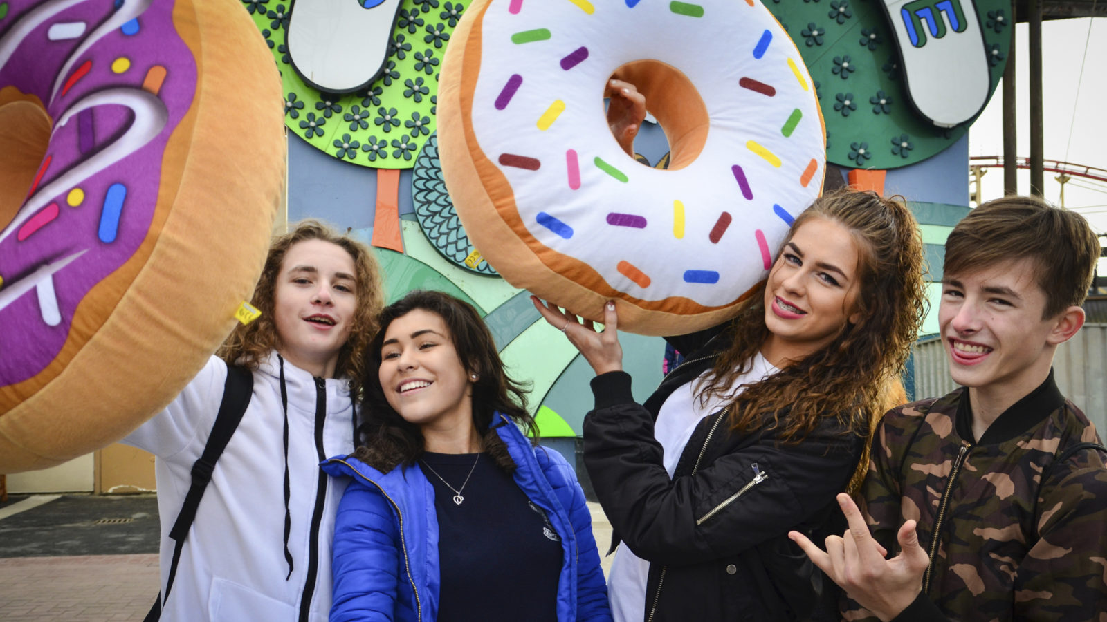 A group of four teenagers, posing for a photograph with two giant doughnut toys.
